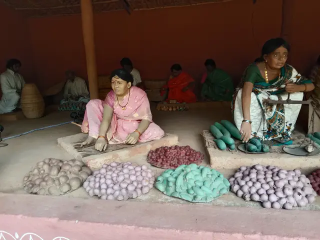 The image shows a group of women sitting on the floor in front of a pile of vegetables, with a wall...