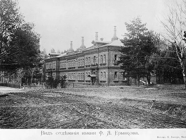 The image shows a black and white photo of a large building with windows, a fence, a group of...