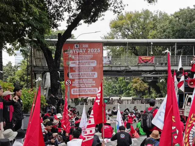 The image shows a large group of people sitting on the ground in front of a crowd, some of them...