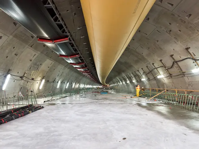 The image shows a large tunnel with a lot of construction equipment inside of it. There are people...