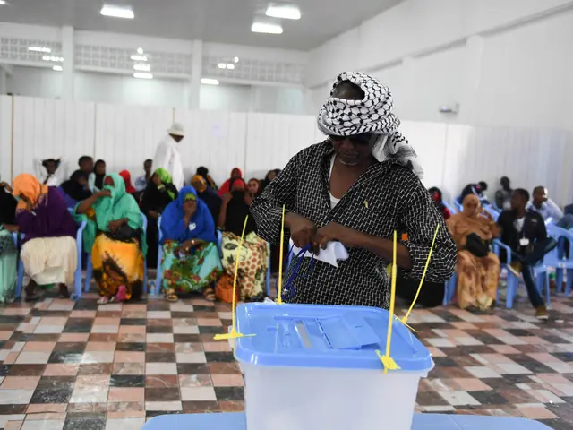 The image shows a woman casting her vote at a polling station in Mogadishu, Somalia. She is...