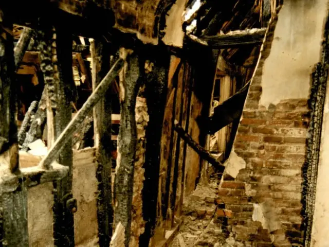 The image shows the interior of a building that has been destroyed by a fire, with wooden sticks...