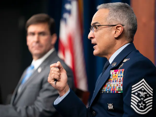 The image shows a man in a military uniform sitting at a table with a pen in his hand, wearing...