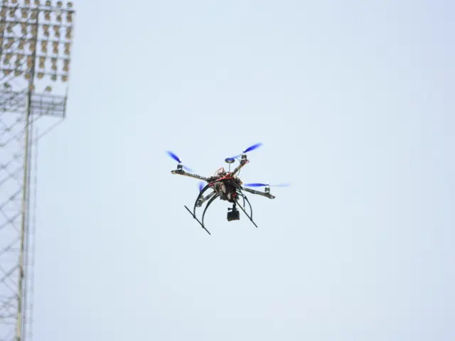 The image shows a drone flying in the air with a tower on the left side and a clear blue sky in the...