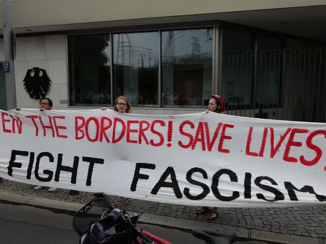 The image shows a group of people holding a banner that reads "Open the Borders, Save Lives, Fight...