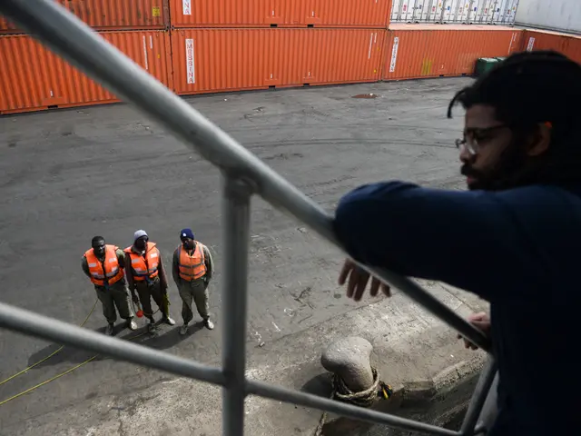 The image shows a man standing on top of a metal railing next to a group of people wearing orange...