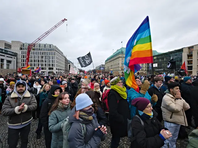 The image shows a large group of people standing in front of a building, holding flags and banners...