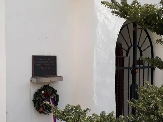 The image shows a white building with a wreath hanging on the side of it, a board with text on it,...