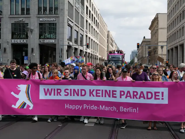 The image shows a group of people walking down a street in Berlin, Germany, holding a pink banner...