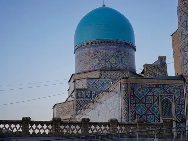 The image shows a mosque with a blue dome on top of it, surrounded by a wall with railings, a pole...