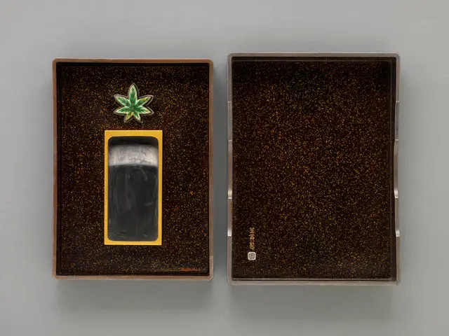 The image shows a black and gold cigarette case with a marijuana leaf on it, sitting on a grey...