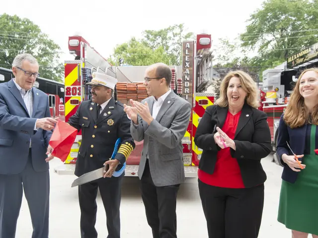 The image shows a group of people standing in front of a fire truck, clapping their hands and...