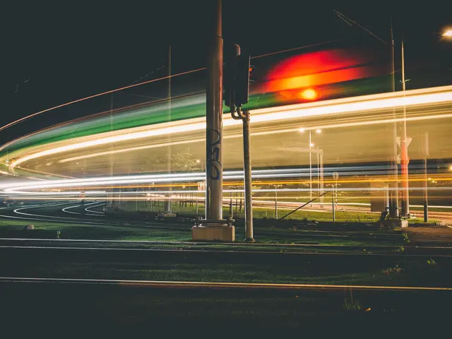 The image shows a long exposure shot of a city street at night, with light trails of cars passing...