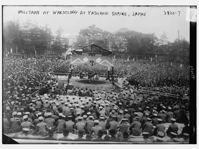 The image shows a black and white photo of a crowd of people watching a wrestling match in Yasukuni...