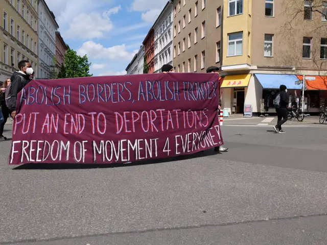 The image shows a group of people walking down a street, holding a banner that reads "Abolish...