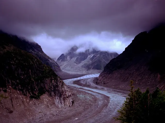 The image shows a large glacier in the middle of a mountain range, surrounded by trees on the right...