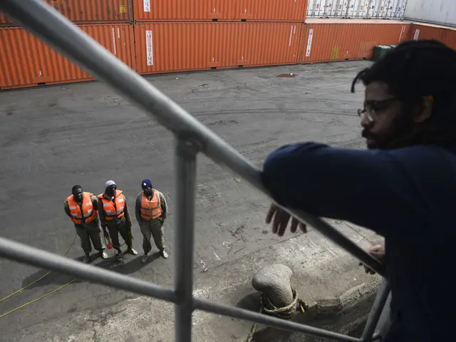 The image shows a man standing on top of a metal railing next to a group of people wearing orange...