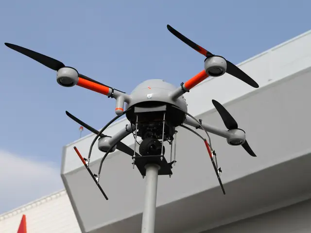 The image shows a drone flying over a building with a pole in the foreground and a clear blue sky...