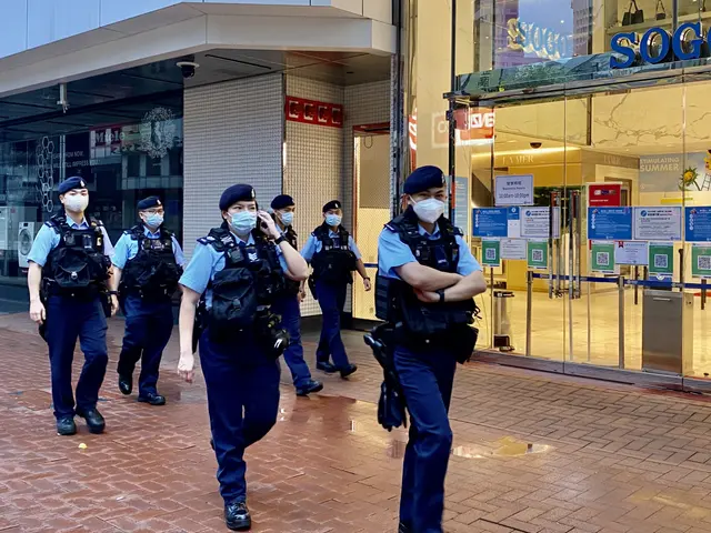 The image shows a group of police officers wearing face masks walking down a street in front of a...