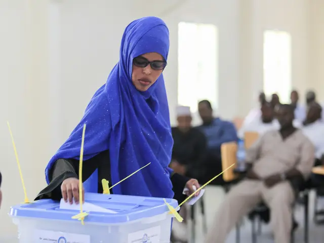 The image shows a woman in a blue headscarf casting her vote at a polling station, surrounded by a...