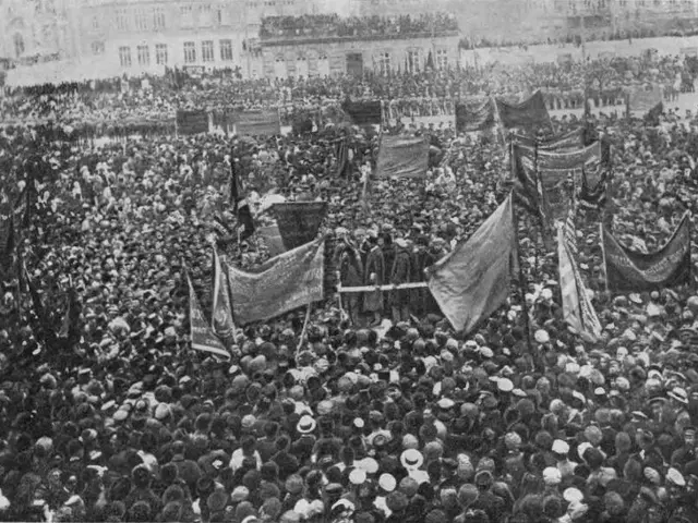 The image shows a large crowd of people standing in front of a building, with flags waving in the...
