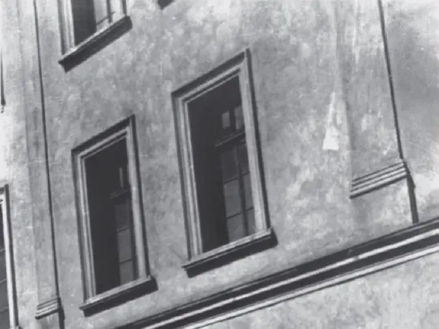 The image shows a black and white photo of a building with windows, doors, and a metal fence. The...