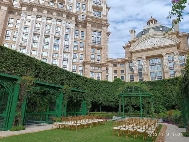 The image shows a wedding ceremony taking place in front of a large building with glass windows,...