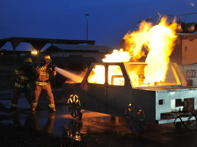The image shows two firefighters wearing helmets and holding pipes in their hands, standing in...