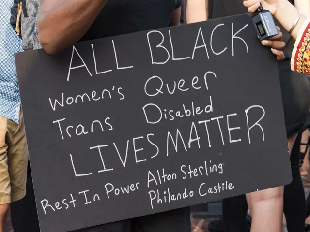 The image shows a group of people standing together, with one person in the center holding a sign...