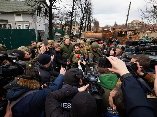 The image shows a group of people standing around each other in front of a crowd of people, some of...