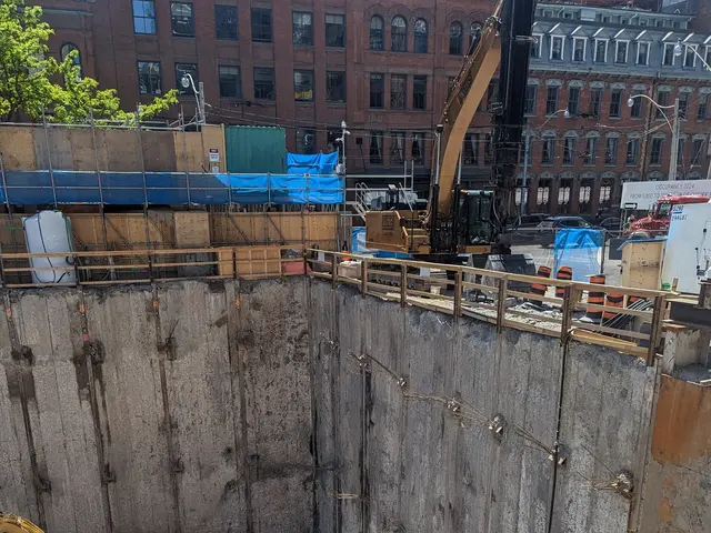 The image shows a construction site with a large hole in the middle of it, surrounded by cranes,...