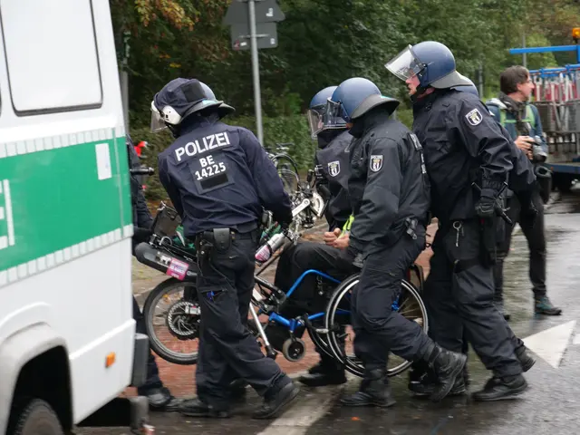 The image shows a group of police officers in riot gear walking down a street next to an ambulance....