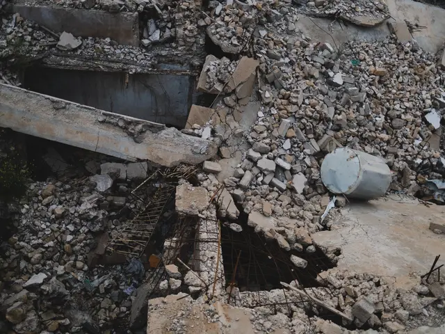 The image shows a collapsed building with a large hole in the middle of it, surrounded by stones,...