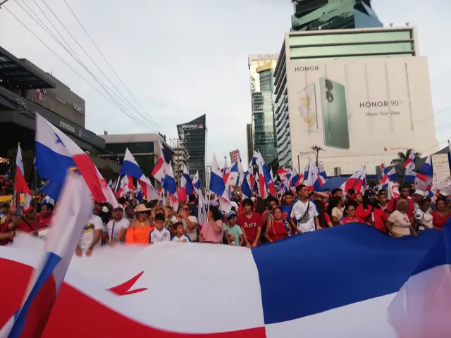 The image shows a large group of people holding flags and banners in the middle of a street,...