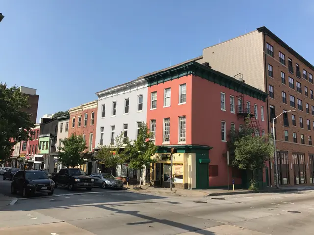 The image shows a city street with cars parked on the side of it, trees lining the street, light...