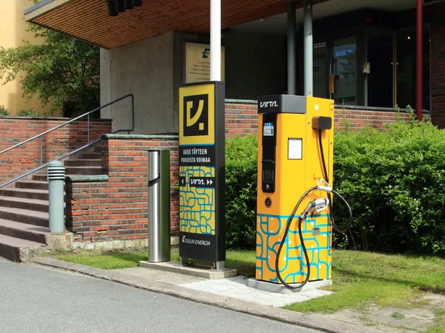 The image shows an electric vehicle charging station on the side of a road, surrounded by grass,...