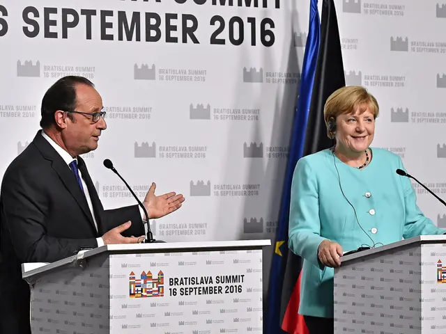 The image shows German Chancellor Angela Merkel and French President Francois Hollande standing in...