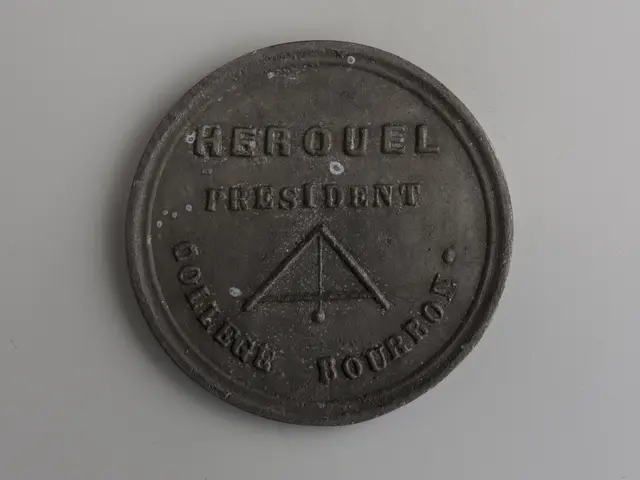 The image shows a black coin with the words "Herouel President" inscribed on it against a white...
