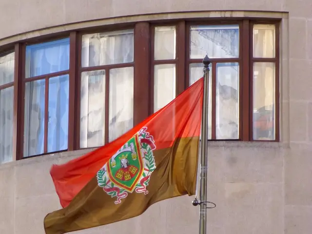 The image shows a building with glass windows and a flagpole flying the flag of Portugal in front...