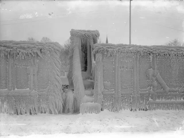 The image shows a black and white photo of a building covered in ice, with trees, poles, and wires...