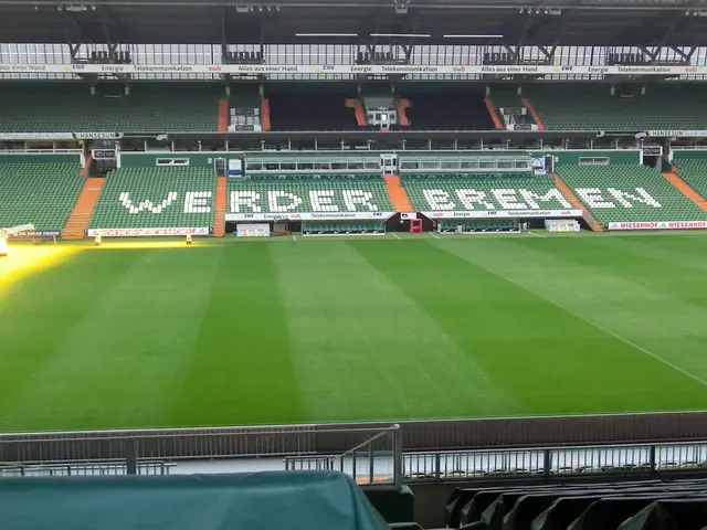 The image shows a large stadium with a green field in the middle of it, surrounded by chairs,...