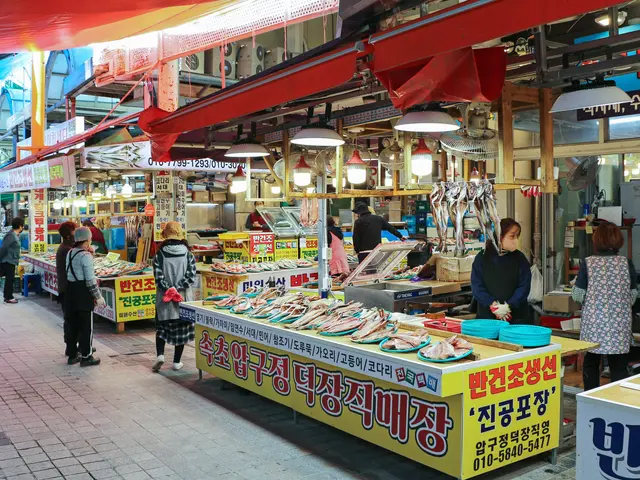 The image shows a bustling street market in Seoul, South Korea. There are many people walking...