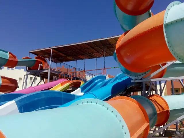 The image shows a large water park with multiple colorful water slides in the middle of it,...