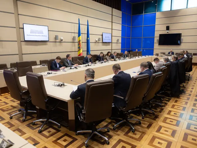 The image shows a large group of people sitting around a long table with microphones, papers, and...
