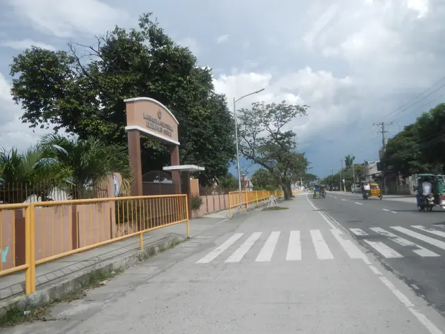 The image shows a city street with vehicles driving on it, a zebra crossing, an arch with text on...