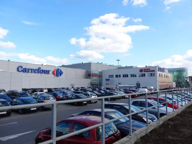 The image shows a large car dealership with cars parked in front of it, surrounded by buildings,...