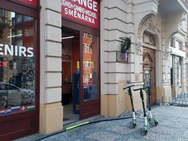 The image shows a city street with a row of scooters parked on the side of it. The street is lined...