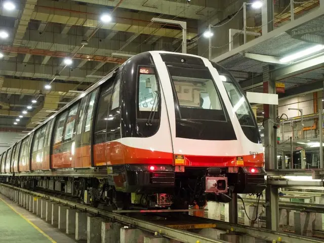 The image shows a red and white train traveling down train tracks inside of a building, with a...