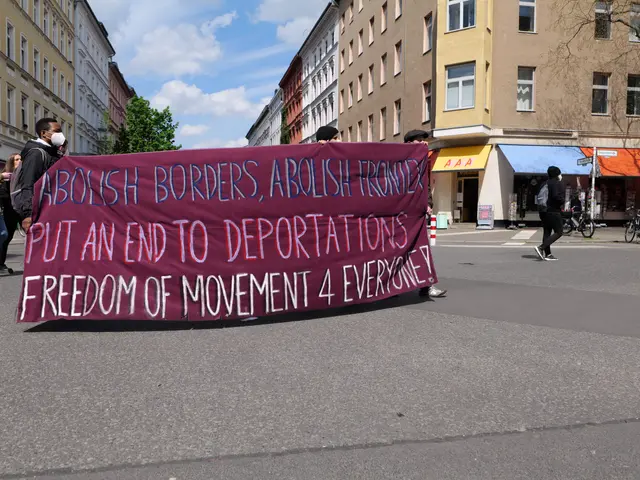 The image shows a group of people walking down a street, holding a banner that reads "Abolish...