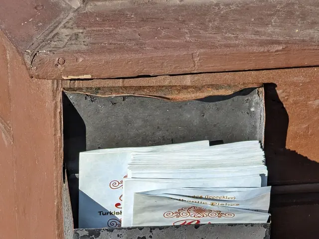 The image shows a metal mailbox on the side of a building, with a few papers inside. The mailbox is...